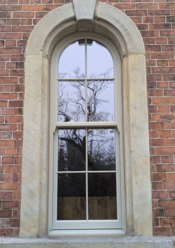 Timber arched casement window with bars inside a grand arched reveal