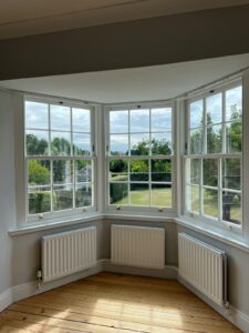 Splay bay window with three sash windows and three radiators with a view of a large field on a summers day
