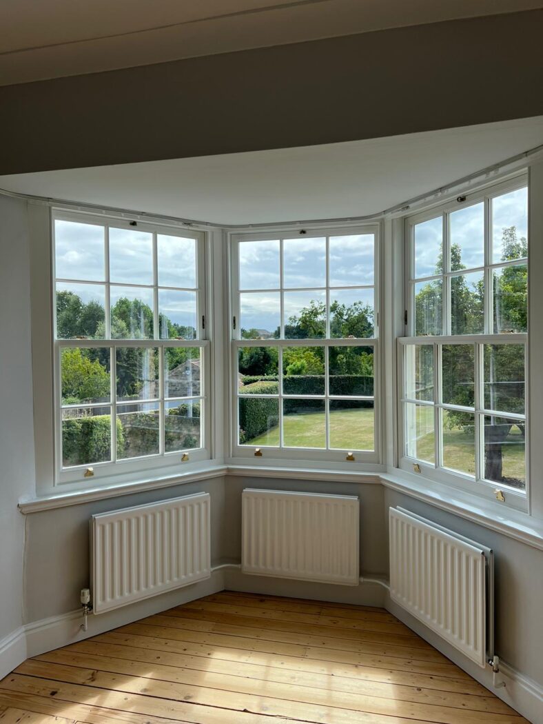 Splay bay window with three sash windows and three radiators with a view of a large field on a summers day