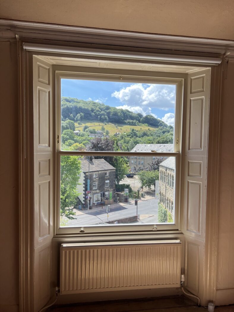 Hardwood Hidden Balance Sash window with wooden panelling at either side. Out of the window Todmorden high street can be seen on a sunny day