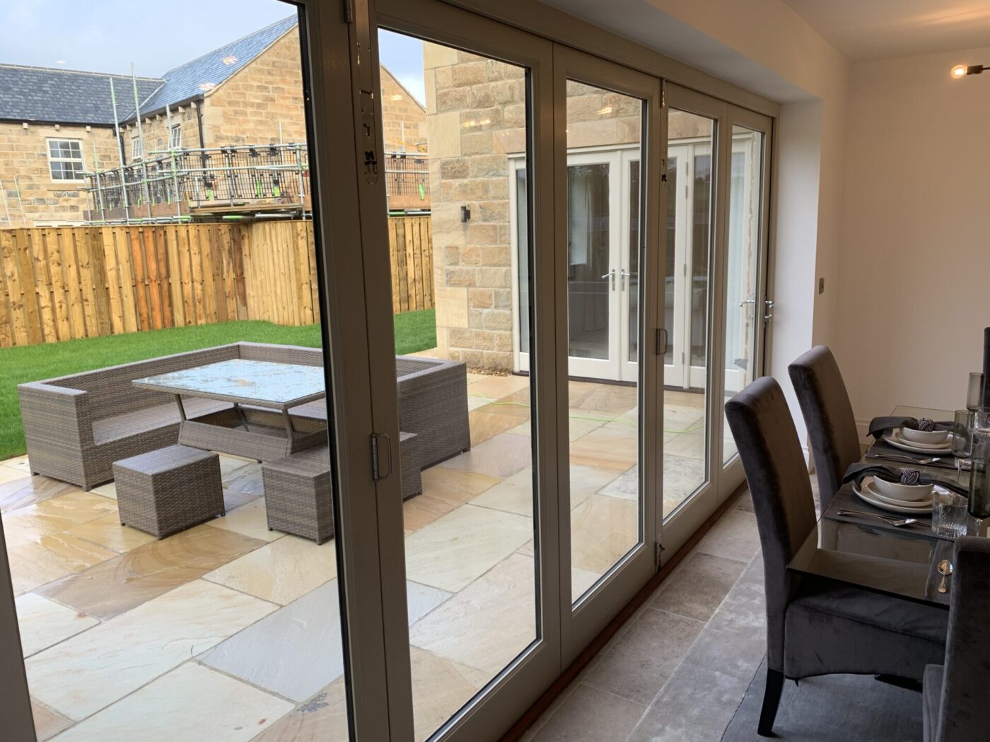 Hardwood white bi fold door separating a dining room and a patio with garden.