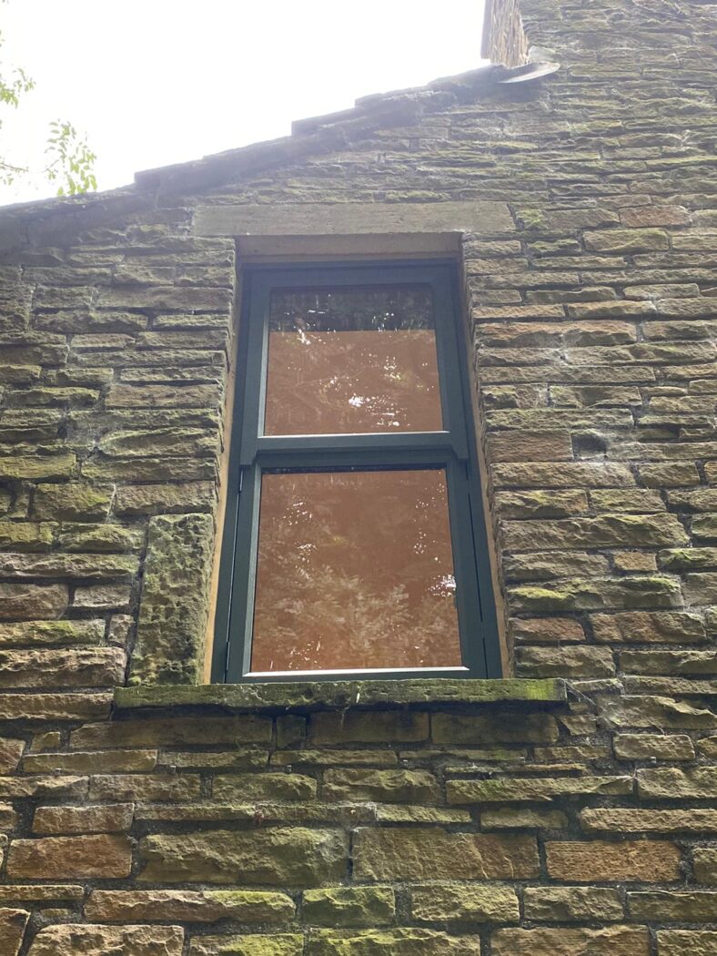Old stone house with a dark grey mock sash window. A soft orange light is coming through the window.
