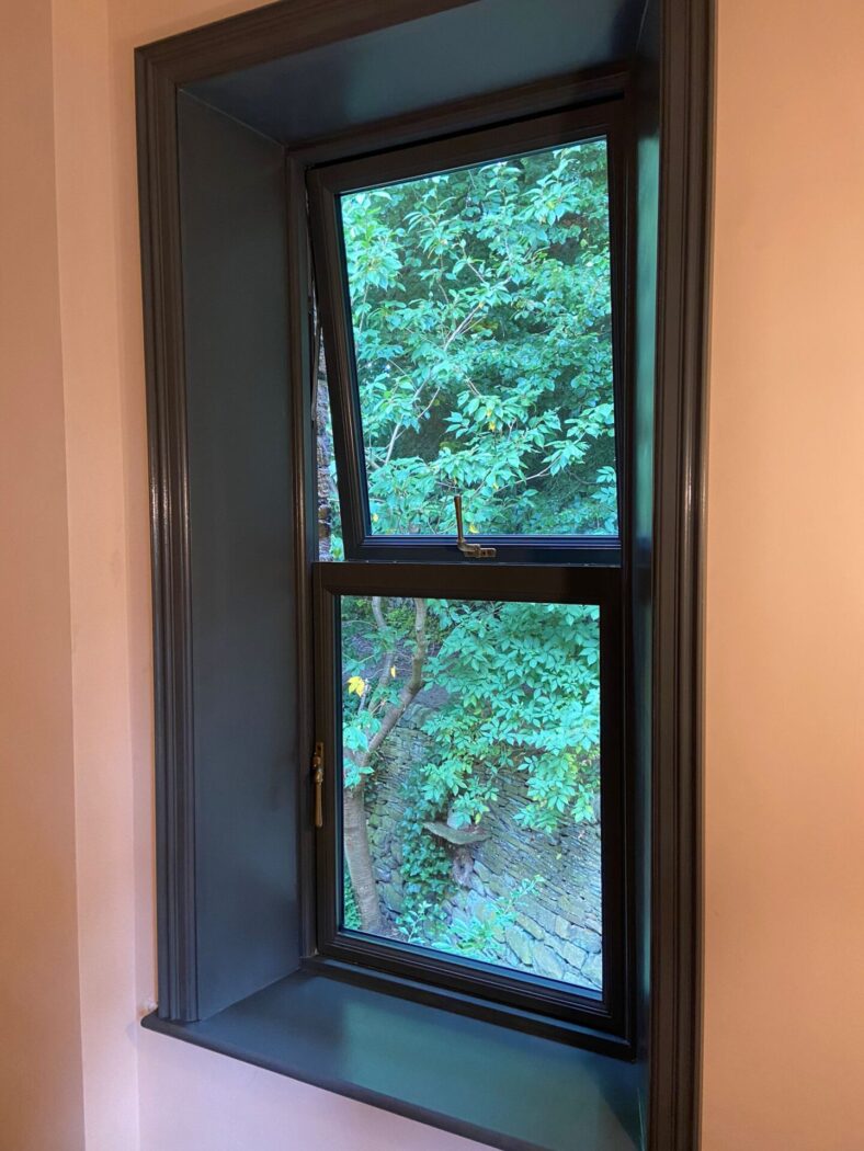 Window frame painted black with a black mock sash window. Th window has a top opening and a bottom opening to comply with safety standards.