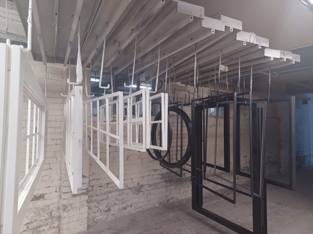 Black and white timber window frames of different shapes and sizes hanging to dry in the Patchett Joinery workshop