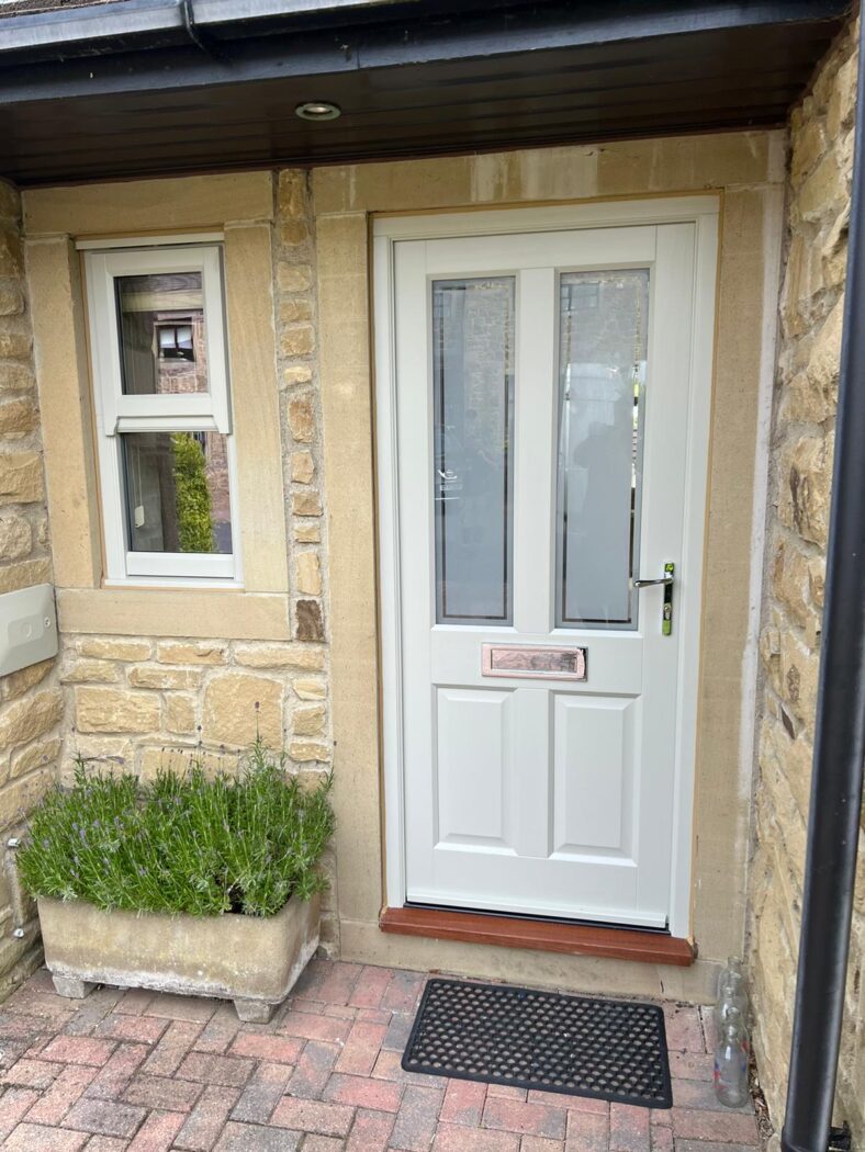 Front porch of a stone house with a cream timber front door, a mock sash window and a planter