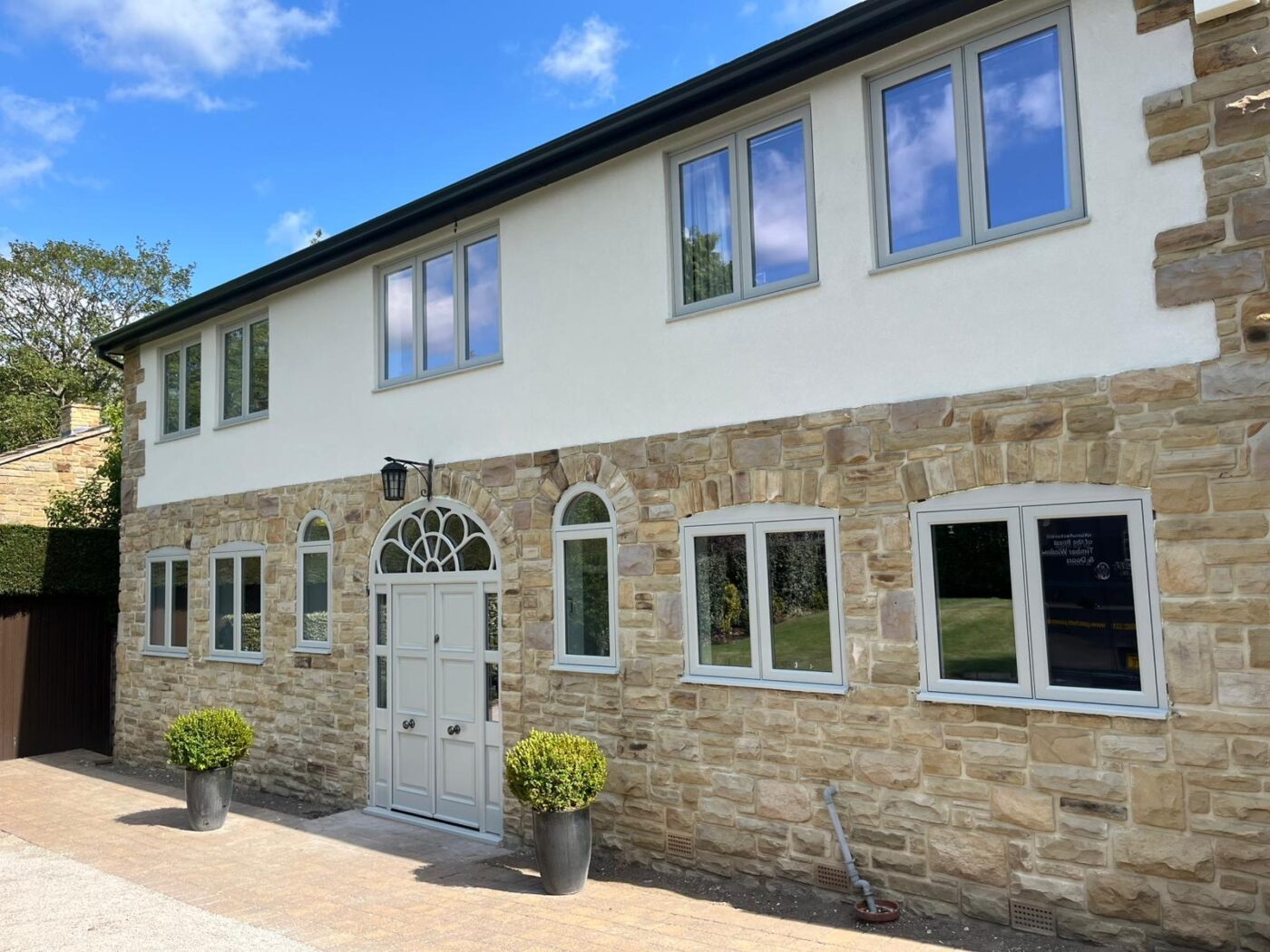 Large house with stone and white washed walls on a sunny with grey flush windows and an ornate door