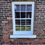The sun is shining on a traditional white sash window with Georgian bars
