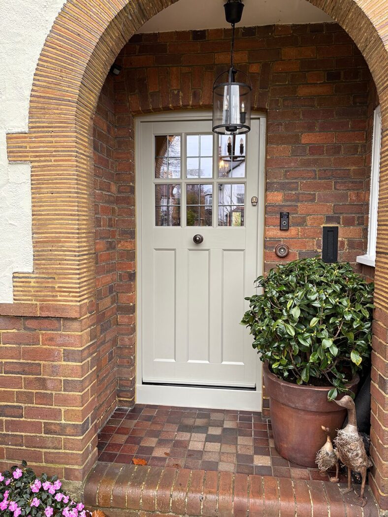 Hardwick white front door with cottage bars inside an arched porch with potted plants.