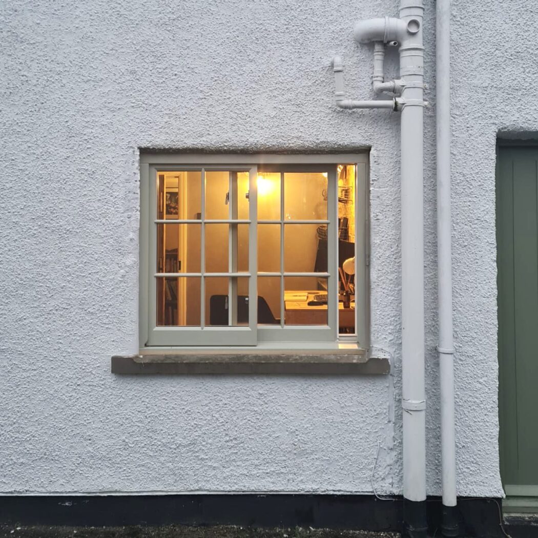 White wash cottage with cosy orange light coming from a wooden pebble grey yorkshire sliding sash window