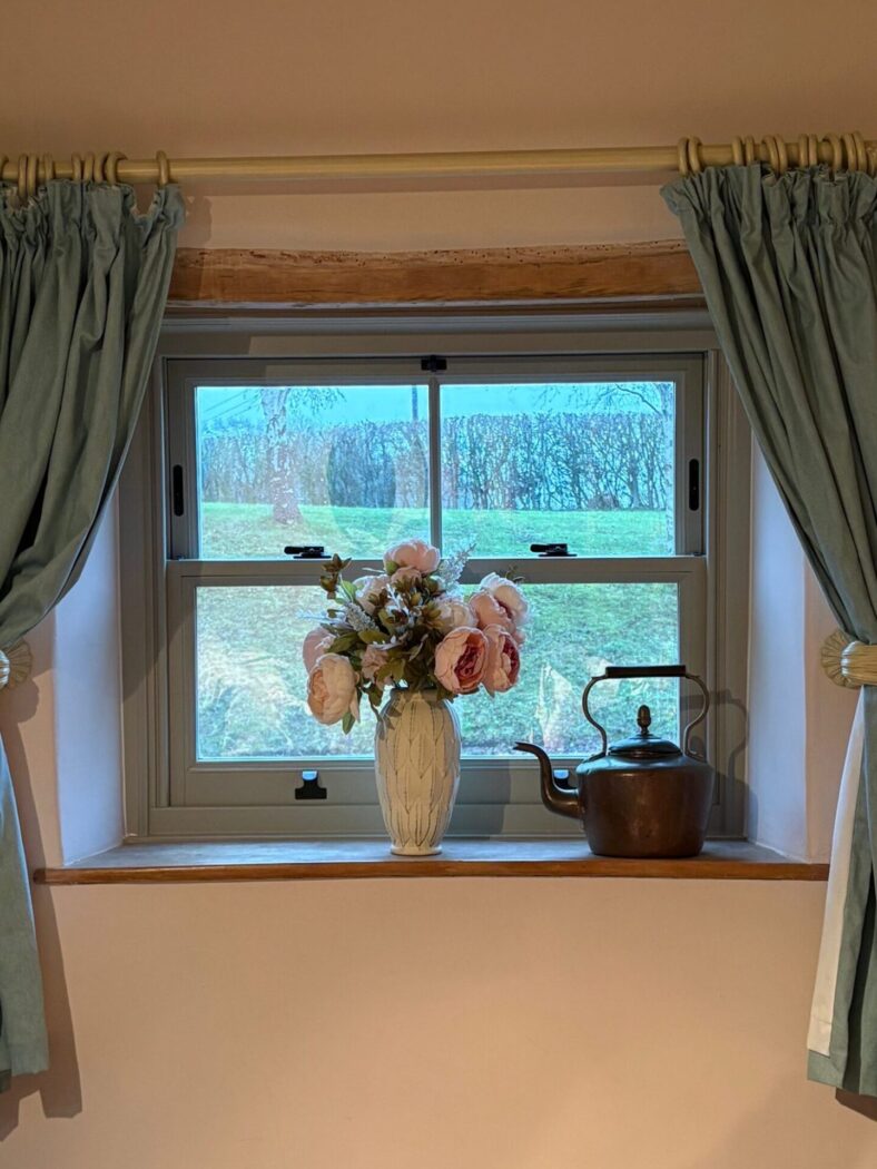 Bedroom sash window in Farrow & Ball Light Grey. On the window sill sits a vase of large pink flowers and vintage copper kettle.