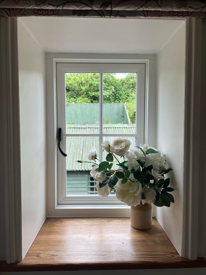 Traditional-style window with a crucifix bar and black iron hardware. The windowl edge has a vase of white flowers