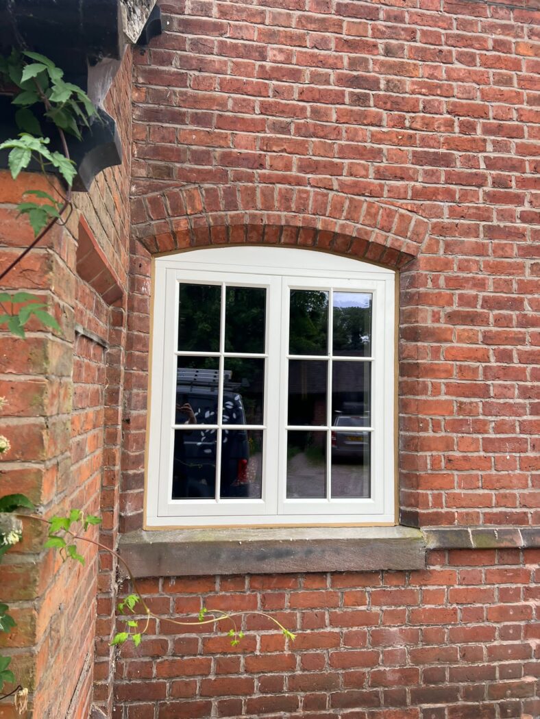 Arched heritage flush casement window with Georgian bars in a red brick house