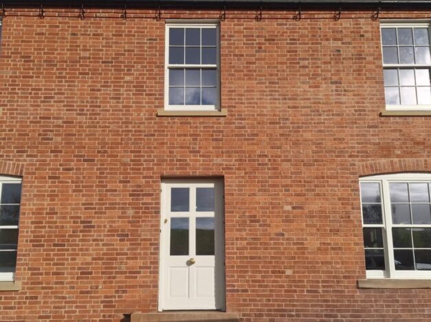 Red brick self-build house with white venetian sash windows and a new timber door
